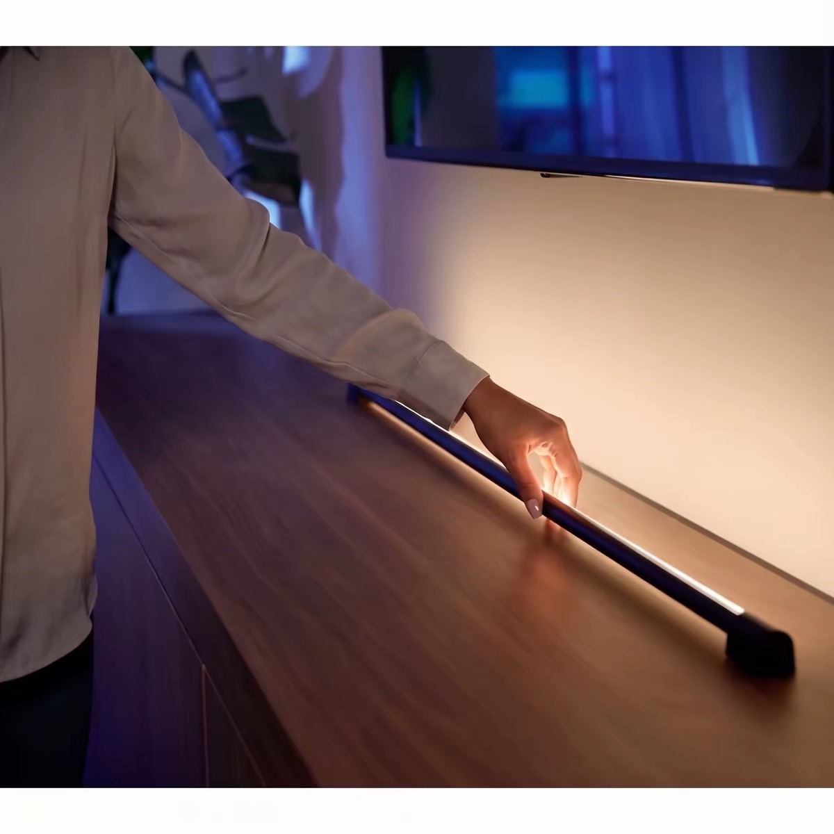 A hand positioning a horizontal light tube on a wooden cabinet